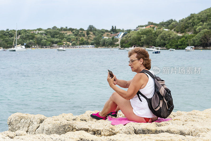 坐在海滩上玩智能手机的资深女性