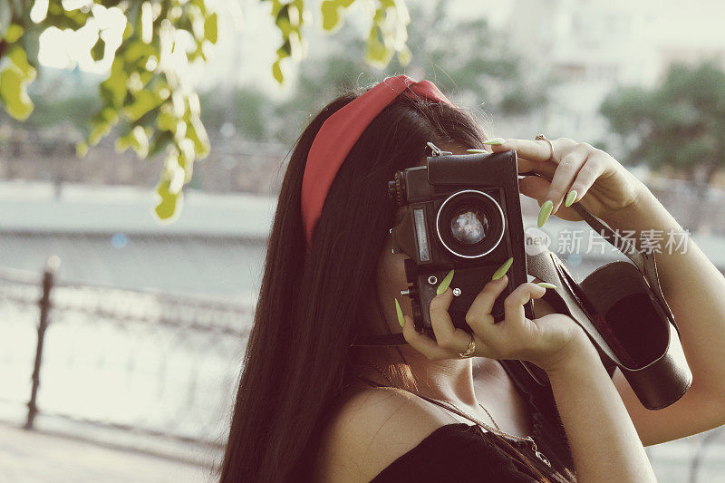 日落时分，带着相机的亚洲女孩在公园里。深色头发的女孩，带着老式胶卷相机