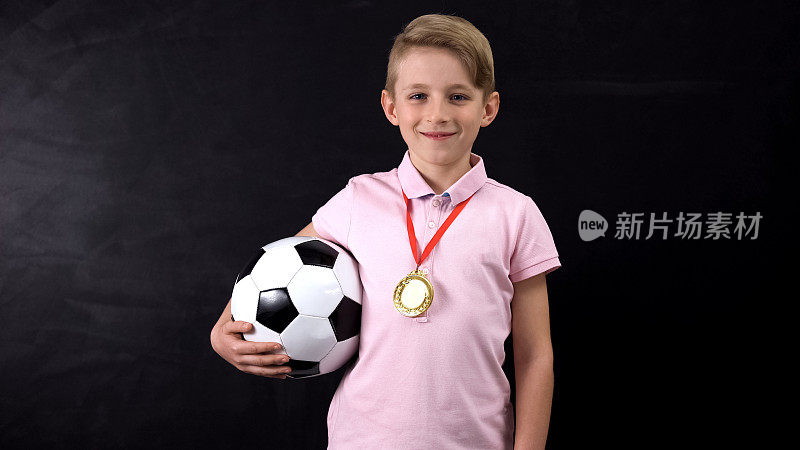 拿着球和奖牌的男孩站在黑板旁边，是足球比赛的获胜者