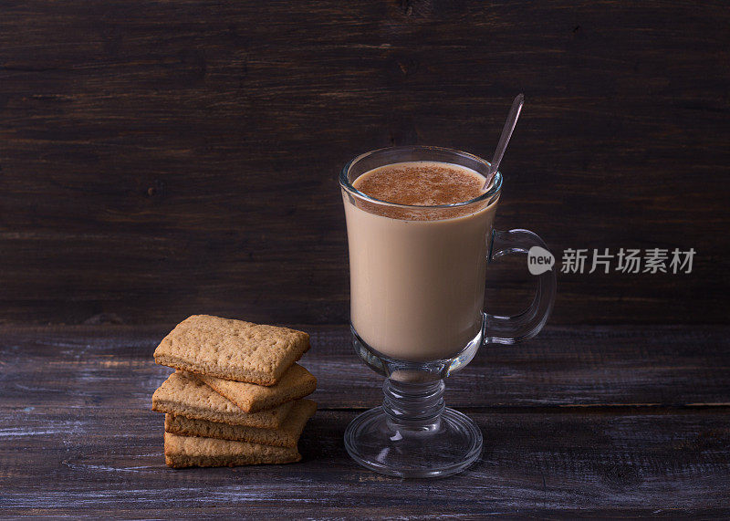 热辣奶茶在玻璃杯中与肉桂，姜饼饼干在木桌上
