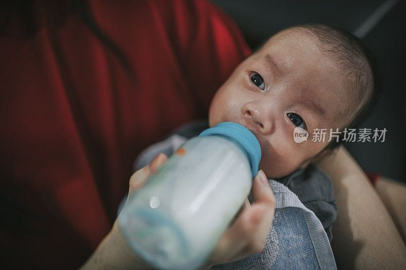 一位亚洲华人祖母正在用奶瓶喂她的孙子