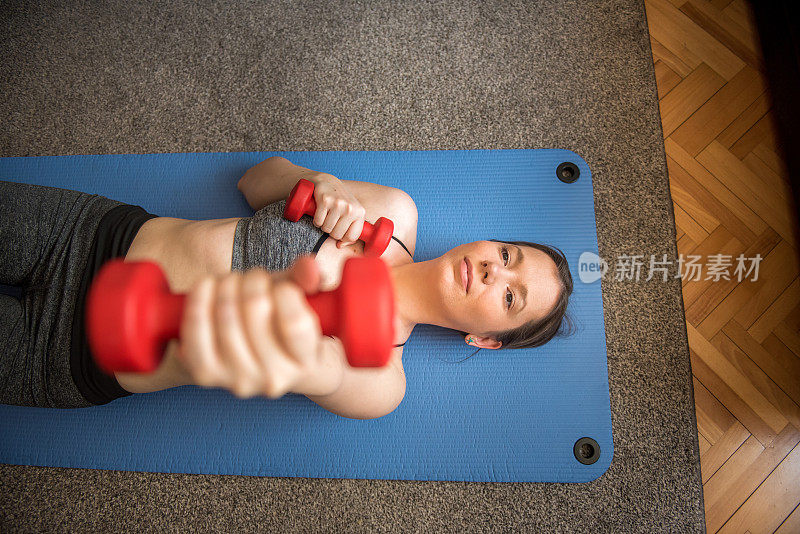 年轻女子在运动垫上躺着用哑铃锻炼