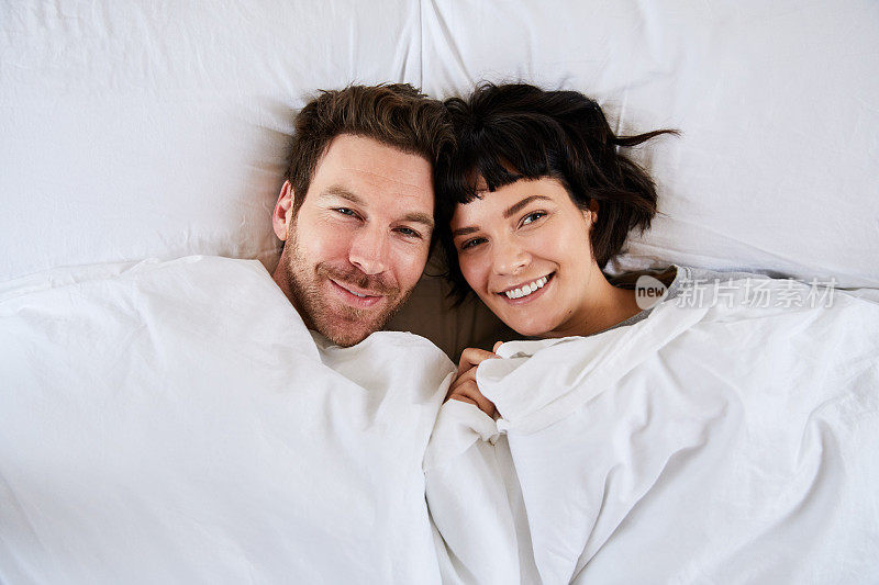微笑的年轻夫妇躺在床上他们的羽绒被