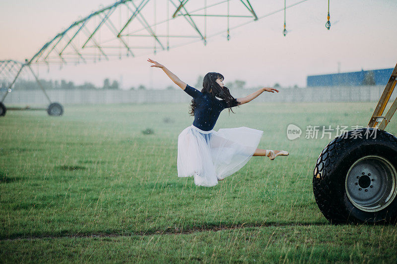 一名芭蕾舞演员在农场里靠近农业喷雾器的轮子跳舞。