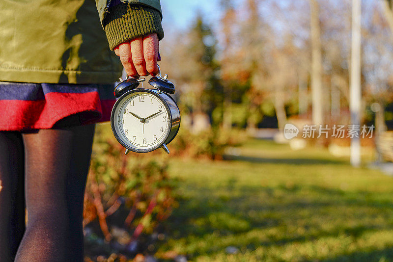 漂亮女人手里拿着闹钟，在户外。生活与享受的概念