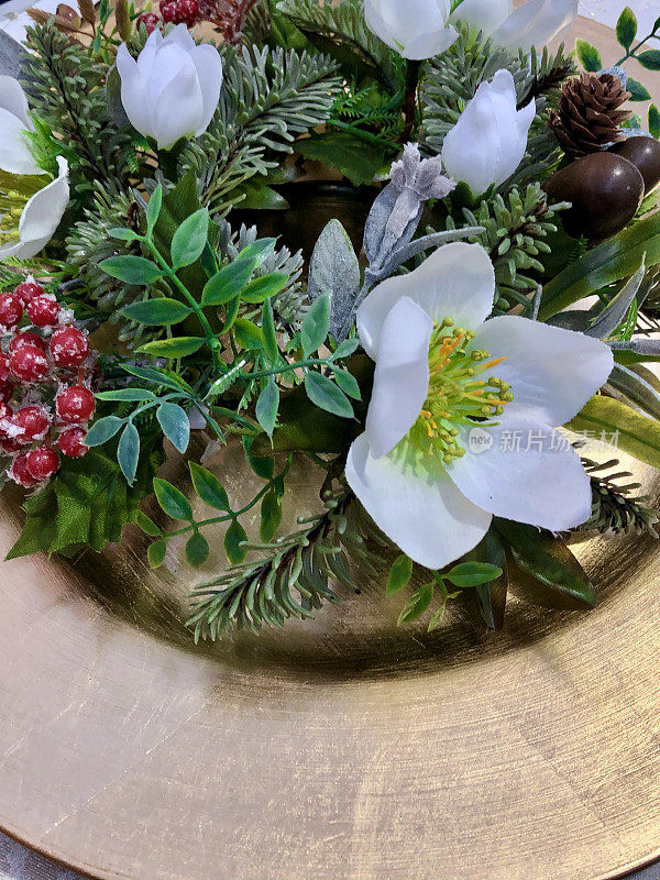 特写图像的一个圣诞桌子的地方设置与人造云杉和冬青花环在金盘上，白色的圣诞玫瑰(Hellebore)花，金桌子runner，上升的观点