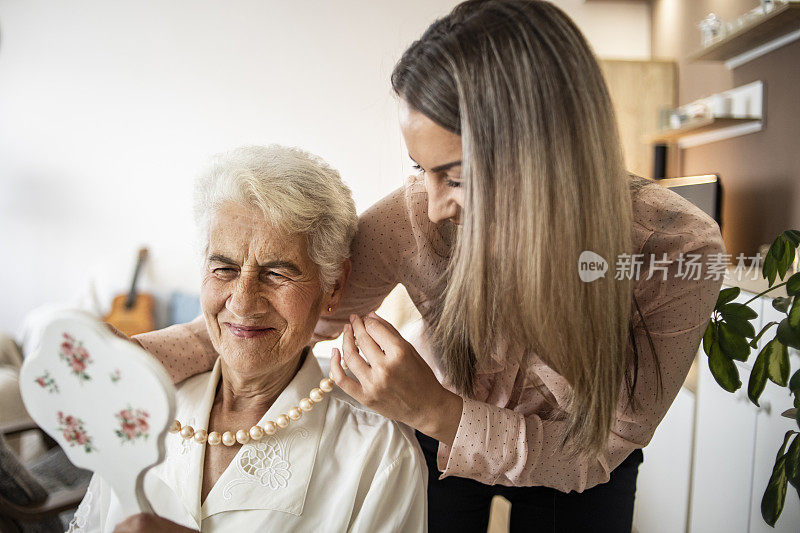 孙女给她的祖母戴上了一条漂亮的项链——一个漂亮的年轻女人在和她的祖母说话——祖母和孙女照镜子