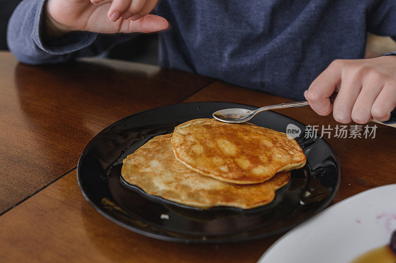 小女孩用手把糖浆洒在煎饼上