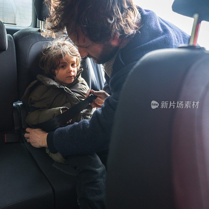 早晨，父亲帮助儿子在汽车后座上系好安全带