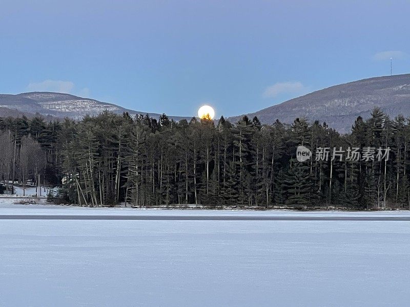月亮升起在高山、树木和冰冻的湖面上