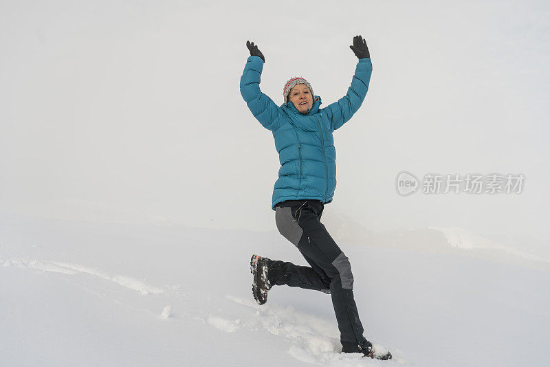 成熟的女人穿着皮大衣在雪地上跳起来