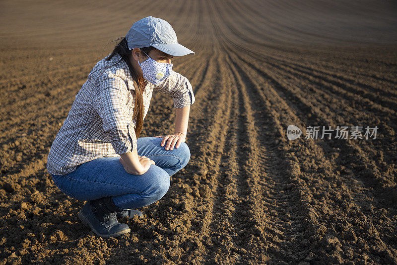 2019冠状病毒病大流行期间，农民戴着防护口罩在工作日结束时检查土壤。