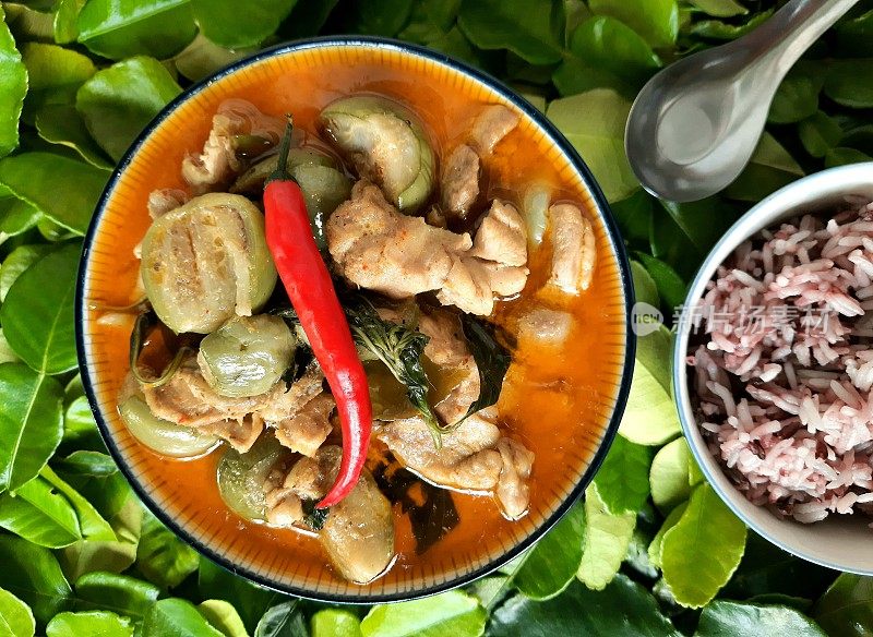 红鸡咖喱汤和糙米-佛手柑叶背景。