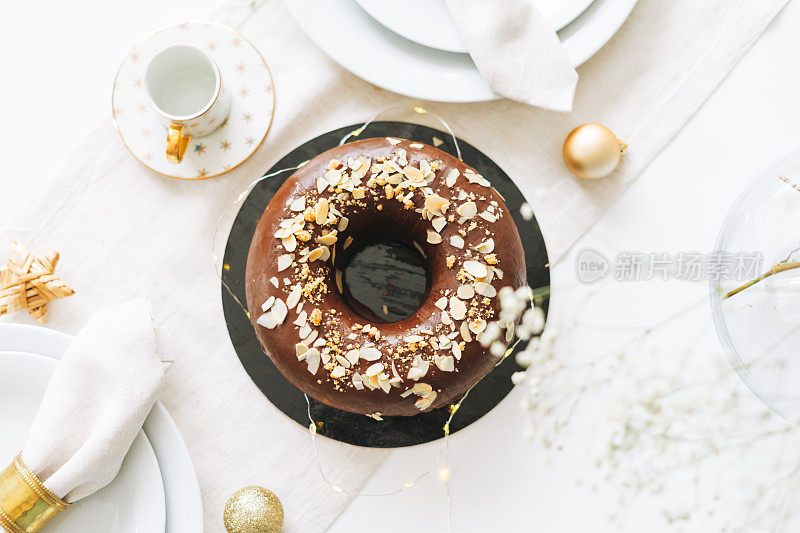 大圆巧克力杏仁蛋糕放在新年的餐桌上，白色的北欧节日餐桌上，俯视图，冬季平摆