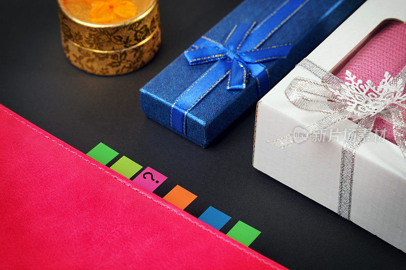 选择礼物的概念。三个不同的礼品盒旁边的日记本上的标签上画着一个问号