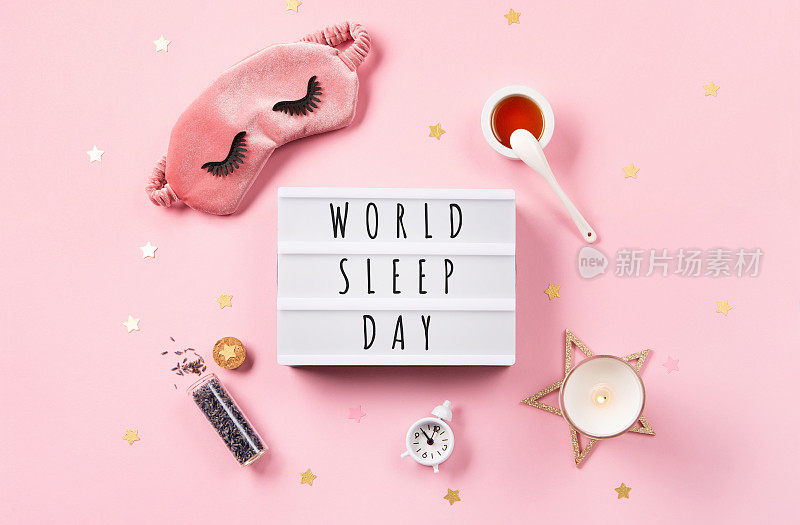 3月18日是世界睡眠日。可爱的睡眠面具和闹钟粉红色粉彩背景，俯视图。