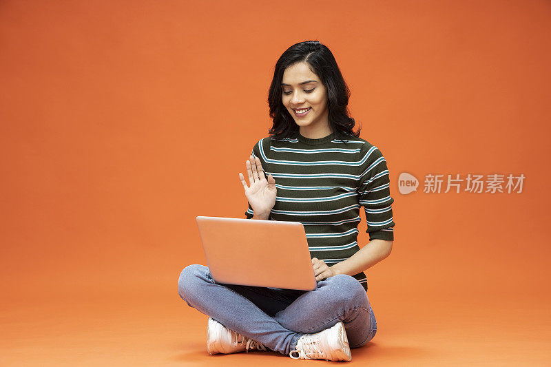 年轻女子坐在地板上，橙色背景的笔记本电脑，库存照片
