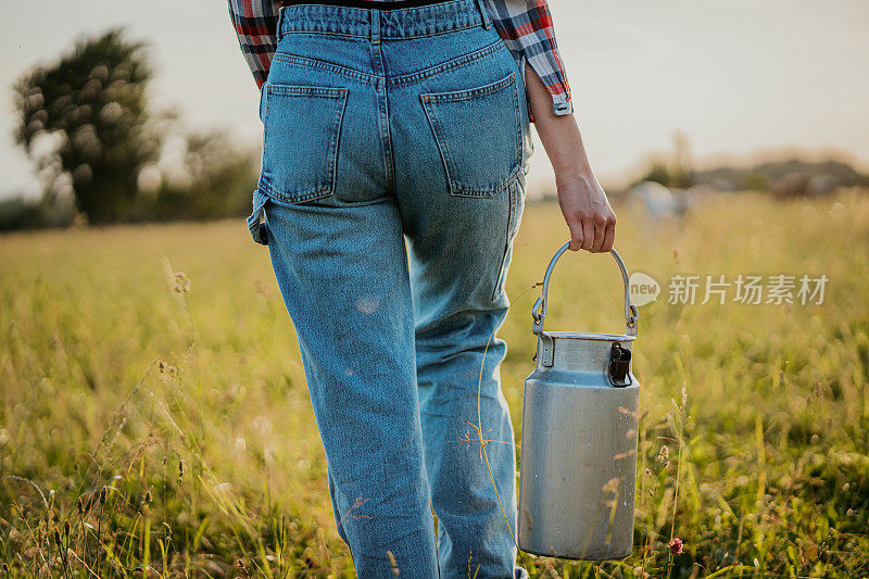 年轻女子手持牛奶罐在田野中行走