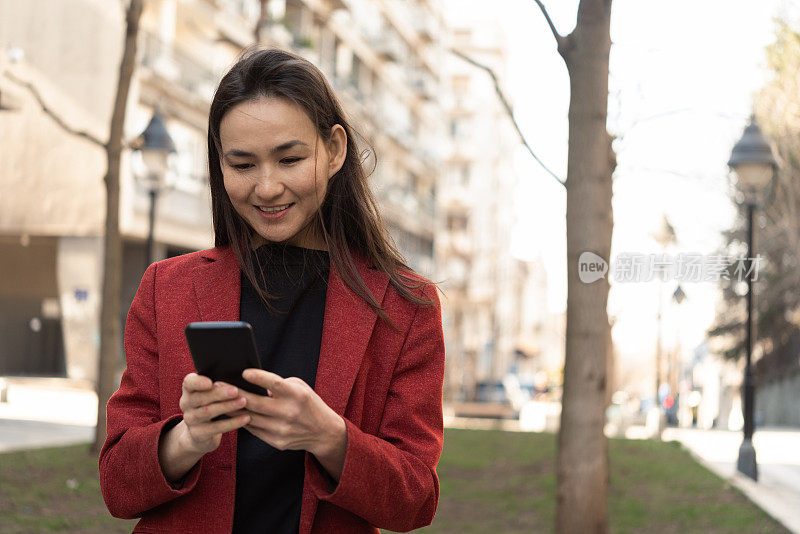 一位亚洲女性一边走路一边使用智能手机