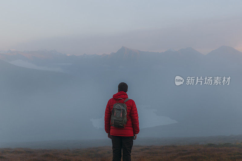 后视图的一个人考虑日落徒步到湖之上的云在挪威山区