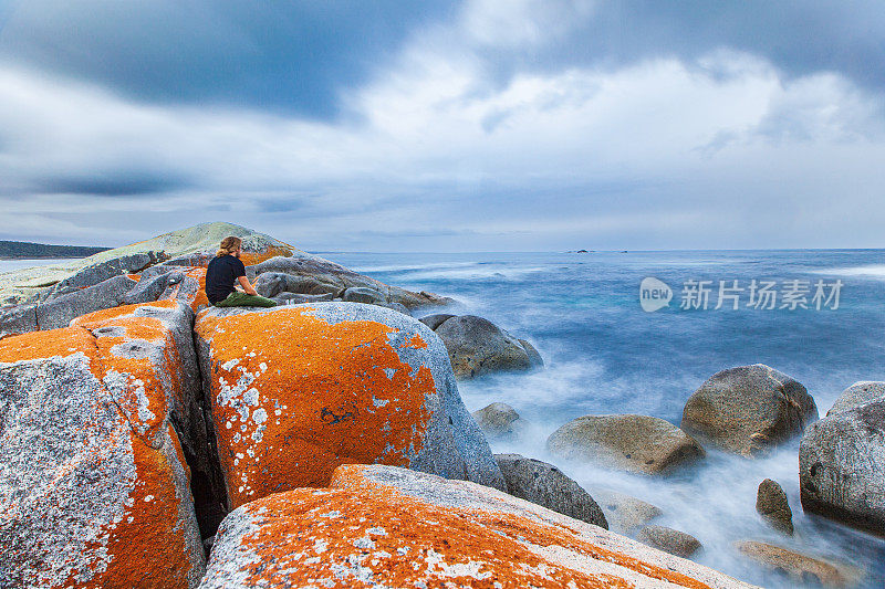 人坐在海边的红色岩石上的海景，天空郁郁寡欢