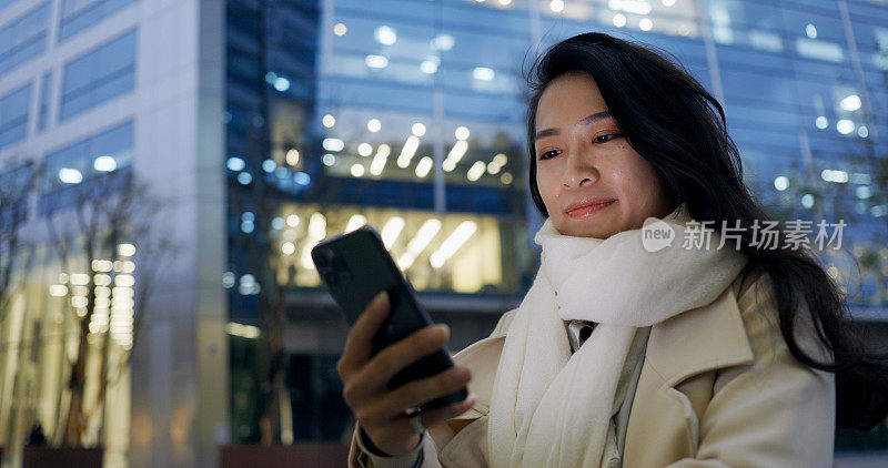 自信的年轻女子在下班的路上使用智能手机在晚上办公大楼外