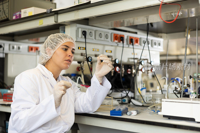 在研究中心工作时，穿着白大褂的专业女生物学家正在试管中检查黄色液体