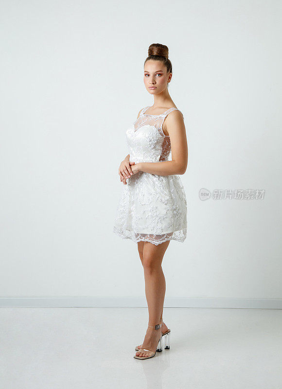 美丽的年轻女子在白色连衣裙与蕾丝覆盖看着相机