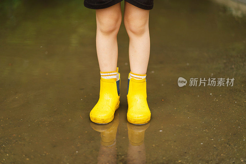 春天的一天，可爱的小男孩穿着雨衣和胶靴走过水坑