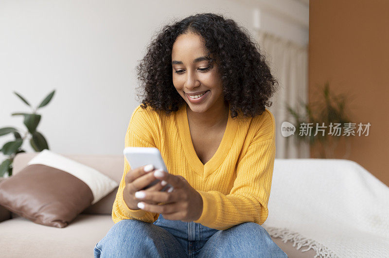 非裔美国妇女使用手机，进行在线视频聊天，坐在沙发上，在社交媒体上发消息