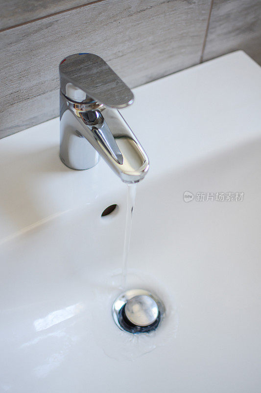 白色陶瓷水槽和镀镍黄铜金属单杆水龙头，水龙头与自来水在浴室。