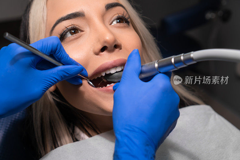 牙医在牙科椅上给女病人钻牙。牙科医生手握器械在病人口腔内进行龋齿治疗的特写