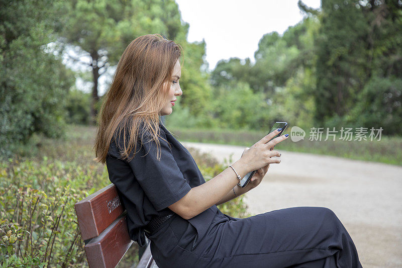 一个女人坐在公园的长椅上摆弄着她的平板电脑