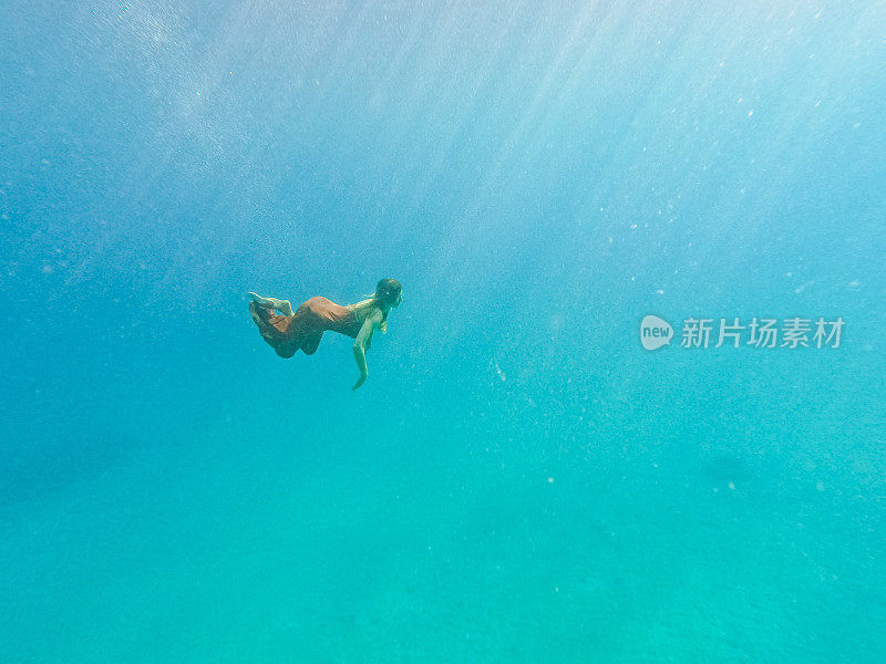 身穿橙色长裙的女子在翠绿的海底潜水，这是用水下相机拍摄的
