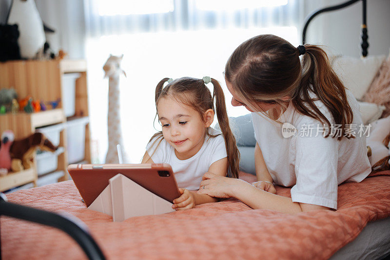 母亲和女儿一起躺在床上看他们的数码平板电脑