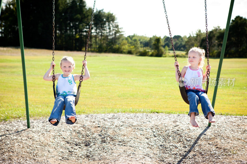 快乐的小双胞胎女孩一起荡秋千在夏天的一天