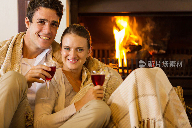 年轻夫妇在壁炉旁喝红酒