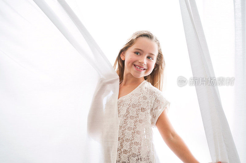 美丽的年轻女孩在白色窗帘中玩耍