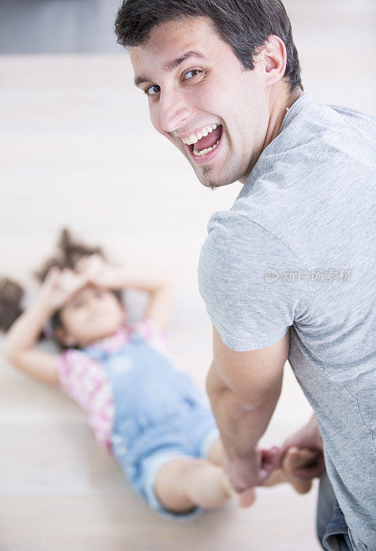快乐的父亲拖着女儿在家里地板上