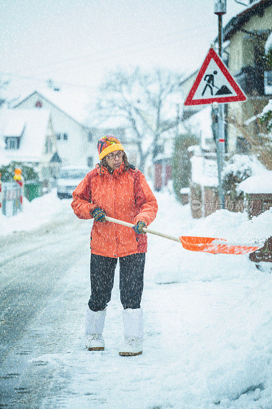 一个成熟的女人在清扫屋前的积雪