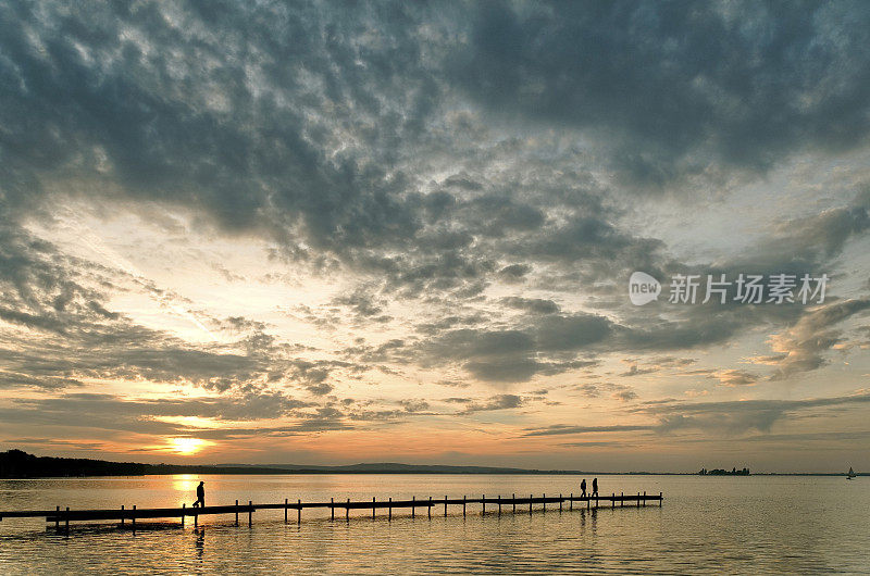 人们在湖边的码头与雄伟的云彩景观在日落