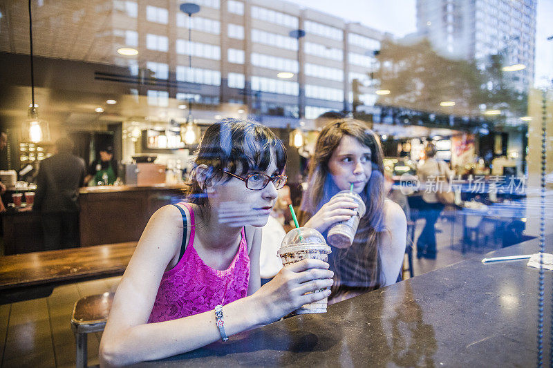 两个十几岁的女孩，姐妹，在一家咖啡馆喝冰咖啡