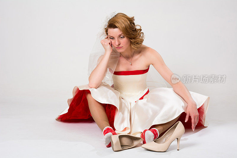 沉思的新娘坐在地板上，袜子靠着