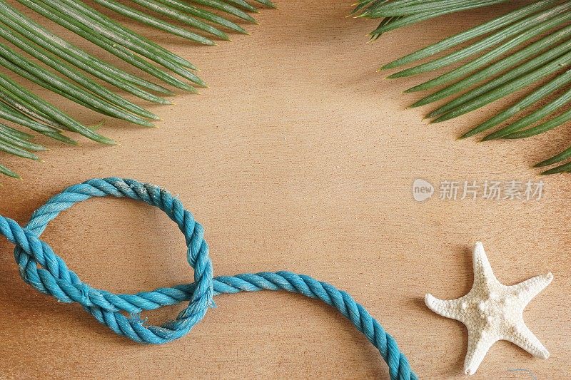 蓝色编织的绳子，棕榈叶和海星躺在一个木制的表面，为你的文本复制空间。