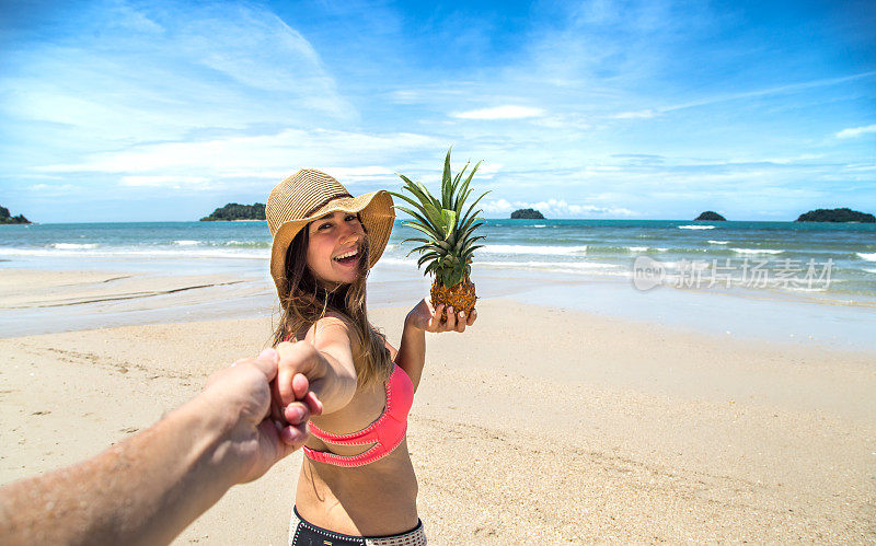 美丽的女孩穿着泳衣和菠萝走在海滩上，牵着男孩的手