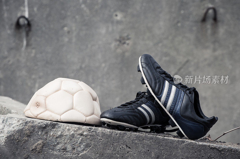 足球鞋和一个球在粗糙的混凝土墙上。