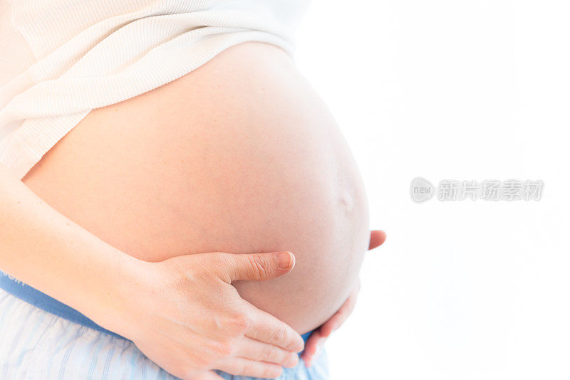 一个孕妇抱着肚子站在窗边