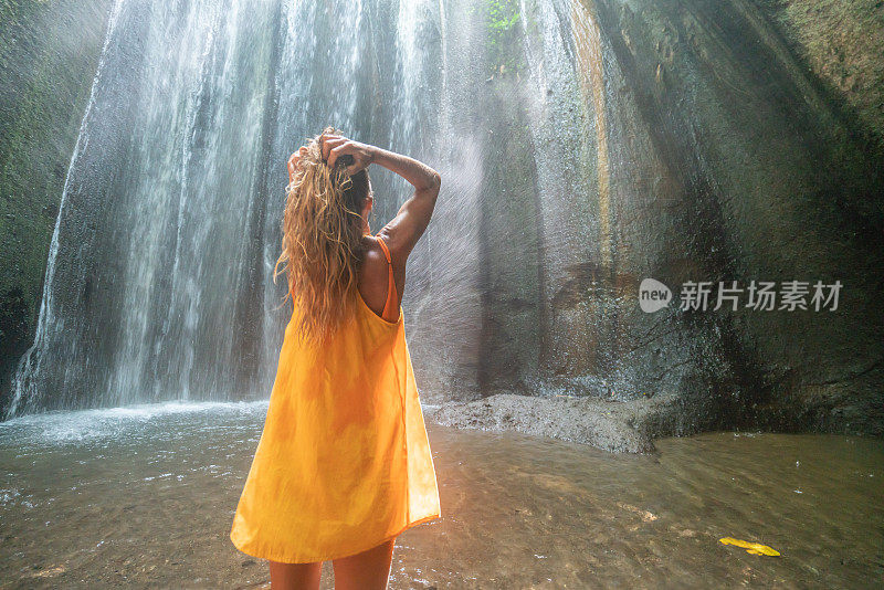 穿着黄色衣服的女孩站在热带雨林的洞穴里，仰望着从岩石上射下来的壮观的阳光。人们旅行的奇妙欲望自然的概念