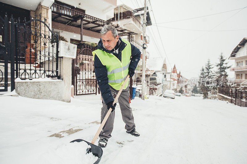 成熟的男人在街上用雪铲清理积雪