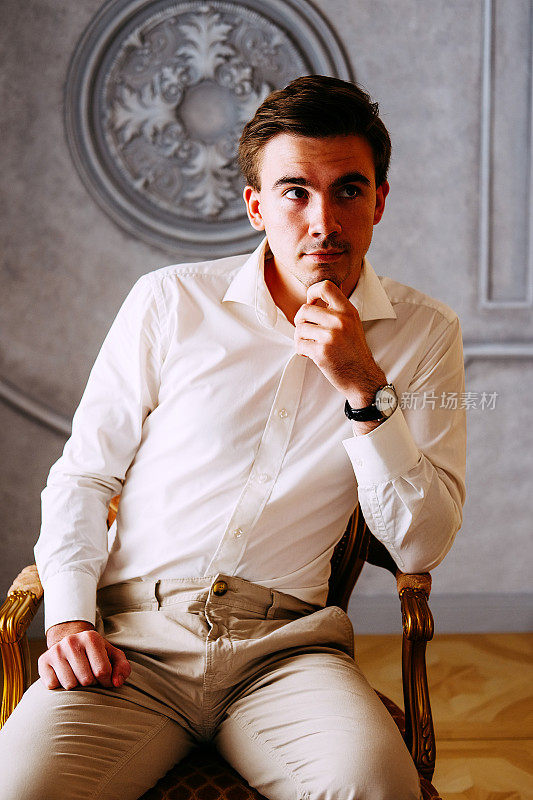 帅气的男子穿着正式的白色衬衫和米色裤子在椅子上等待